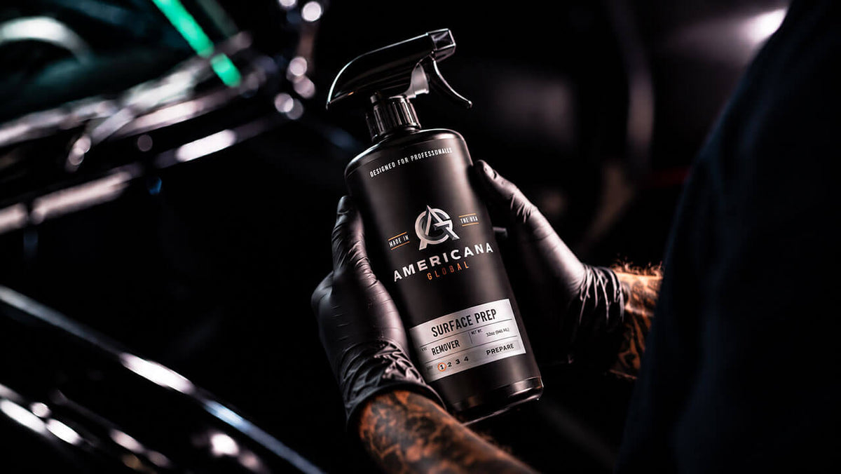Gloved detailer spraying Americana Global Surface Prep on a black vehicle